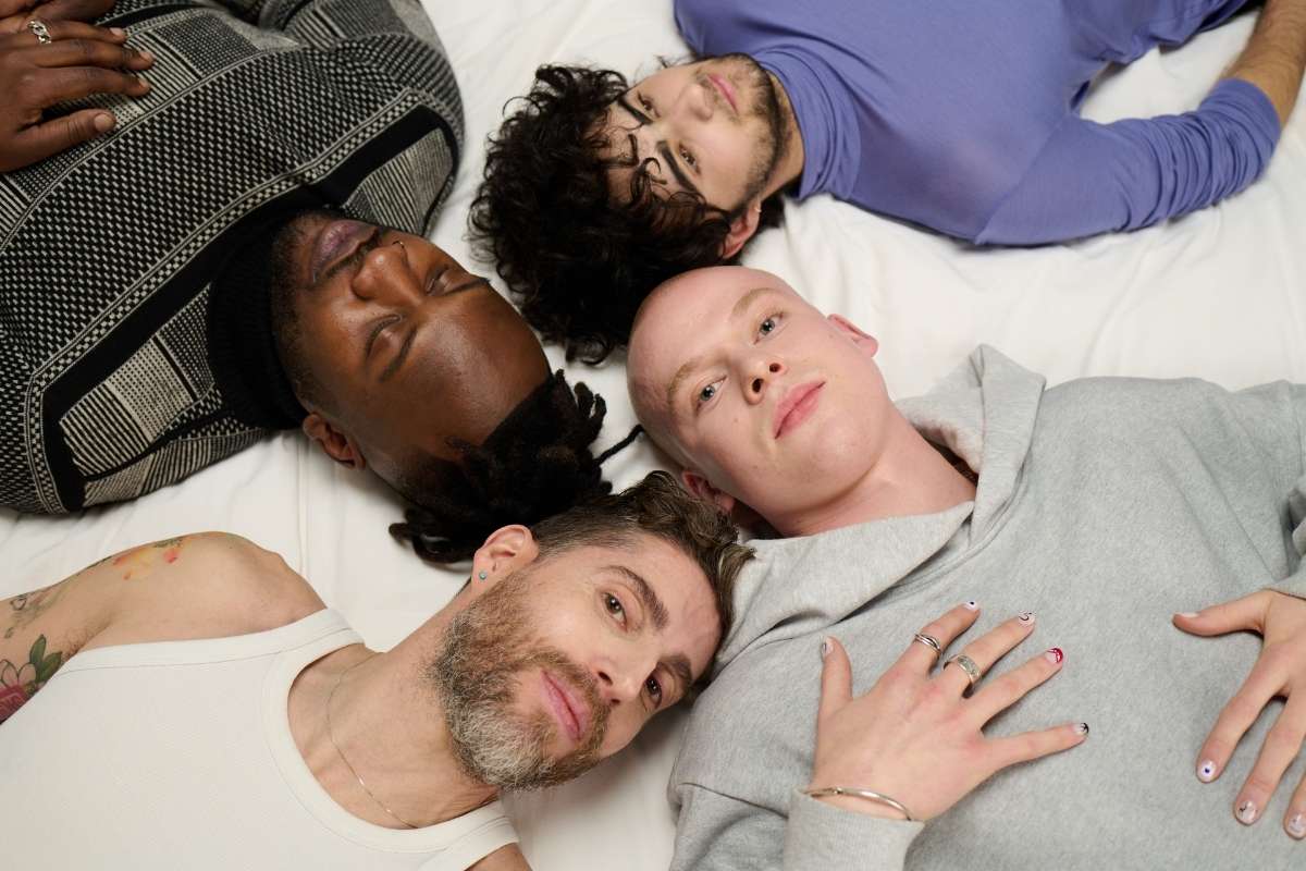Vier Männer liegen Kopf an Kopf auf einem Bett
