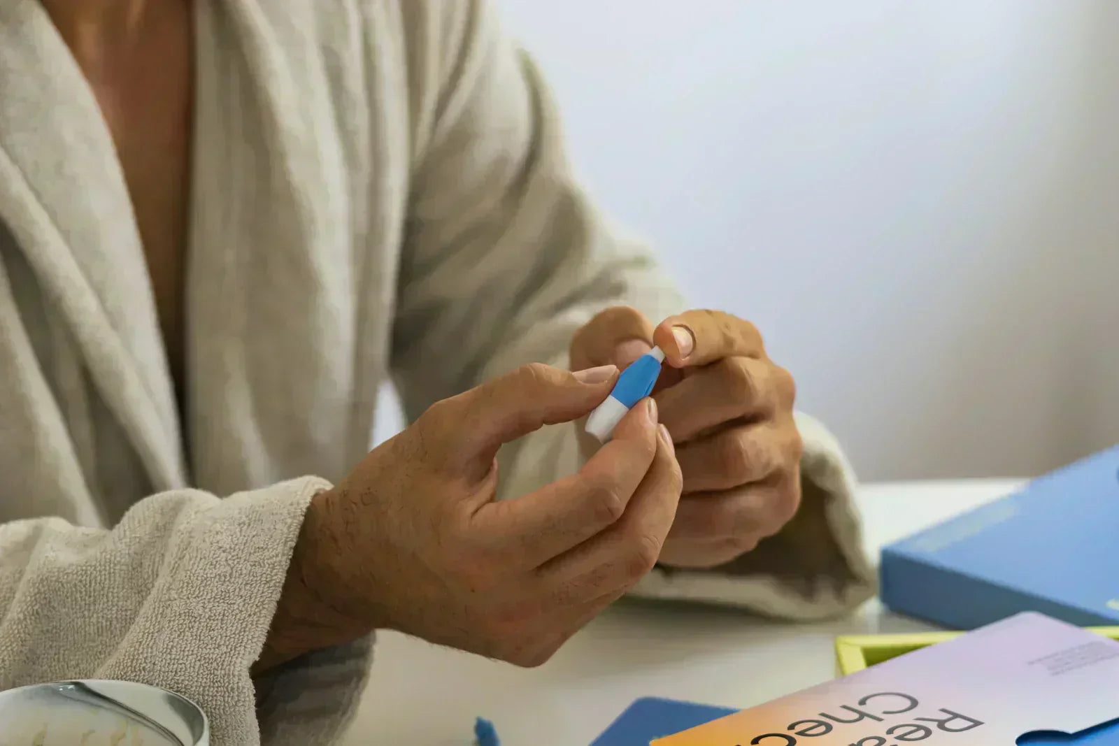 Nahaufnahme von zwei Händen, die eine kleine, blau-weiße Stechhilfe für einen medizinischen Test vorbereiten.