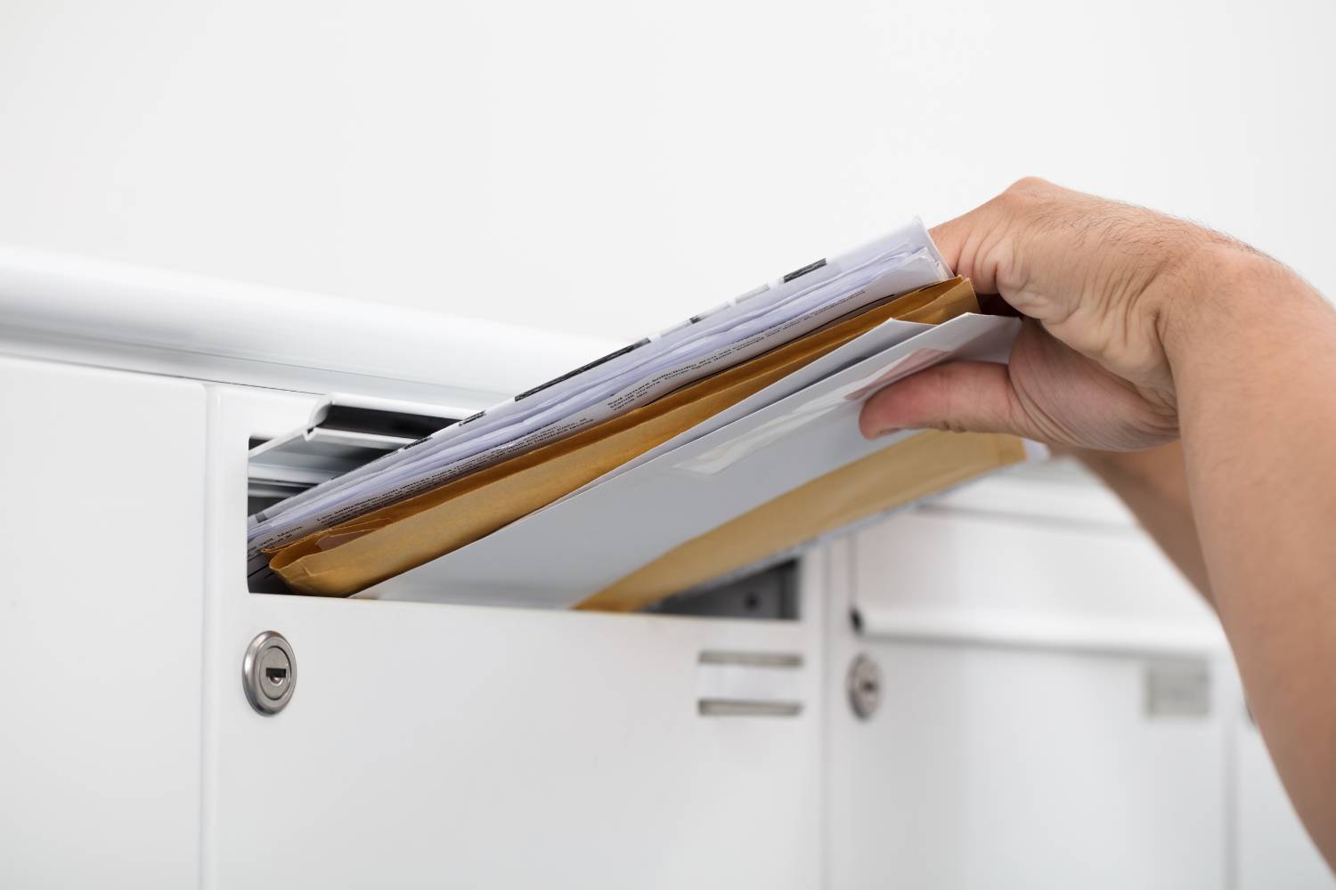 Eine Hand zieht Postumschläge aus einem weißen Briefkasten. Das Bild symbolisiert den diskreten und unkomplizierten physischen Empfang des Medikaments zur Behandlung der erektilen Dysfunktion, nachdem der Online-Prozess abgeschlossen ist.