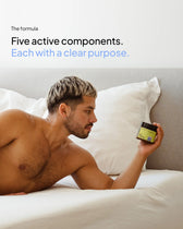 A shirtless man with short, styled blond-highlighted hair lies in a bed with white sheets and pillows, looking at a jar of "Every Health Gut Feeling" supplements held in his hand. The text above reads: "The formula. Five active components. Each with a clear purpose."