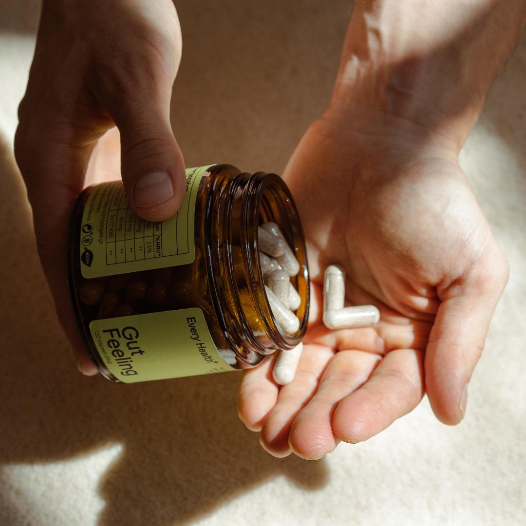 Nahaufnahme von zwei Händen im Sonnenlicht. Die linke Hand hält eine braune Glasdose von Every Health und schüttet mehrere helle „Gut Feeling“ Kapseln in die geöffnete rechte Handfläche.