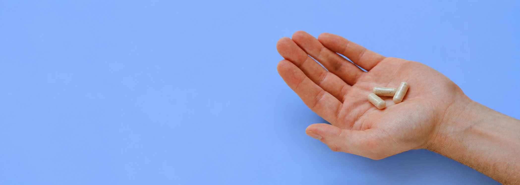 Eine geöffnete Hand hält drei helle „Gut Feeling“ Kapseln von Every Health auf der rechten Seite des Bildes. Der Hintergrund ist einfarbig hellblau.